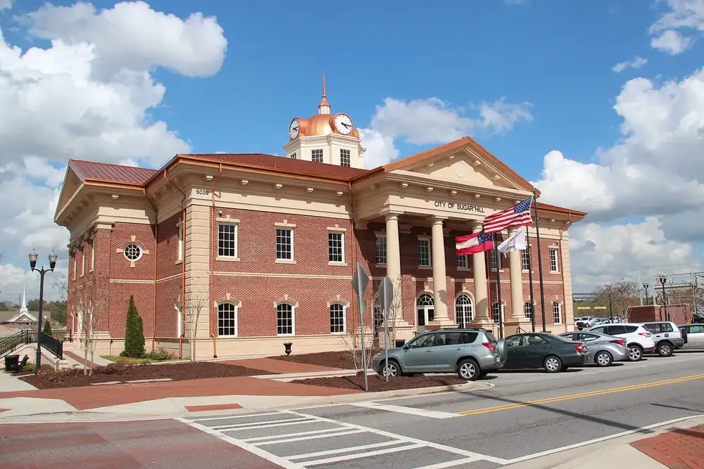 Sugar Hill City Hall, a brick building with columns and a cupola, with flags in Sugar Hill, Georgia